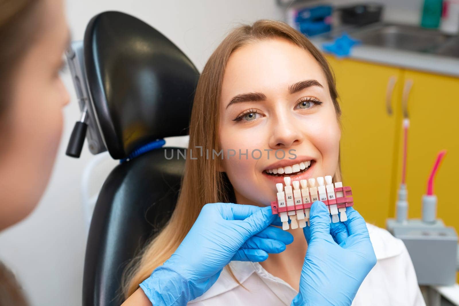 Dentist uses a set of implants with various shades of tone for whitening of teeth to young woman