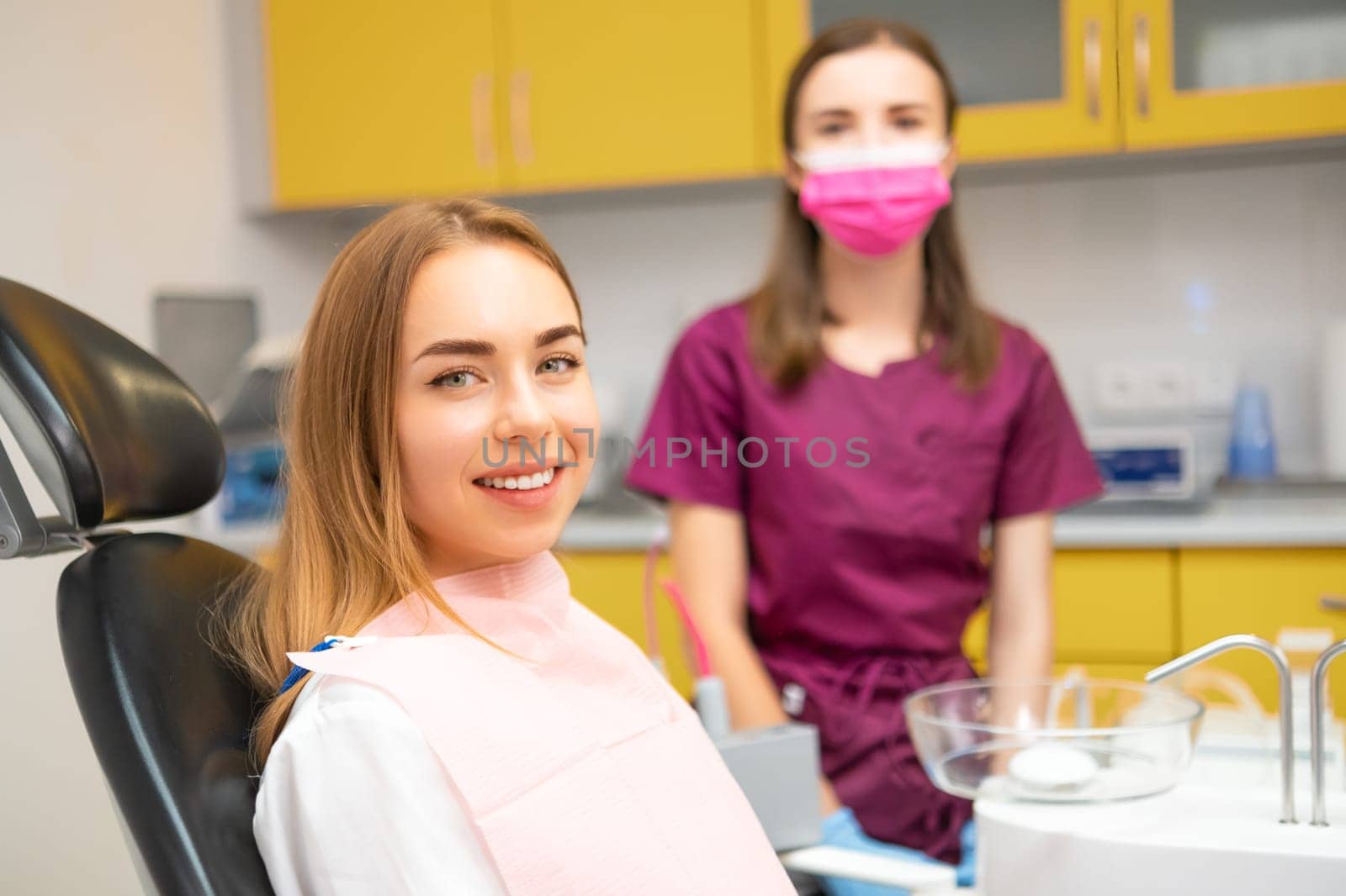 Happy young woman patient smilling sitting in medical chair at dental clinic. by vladimka