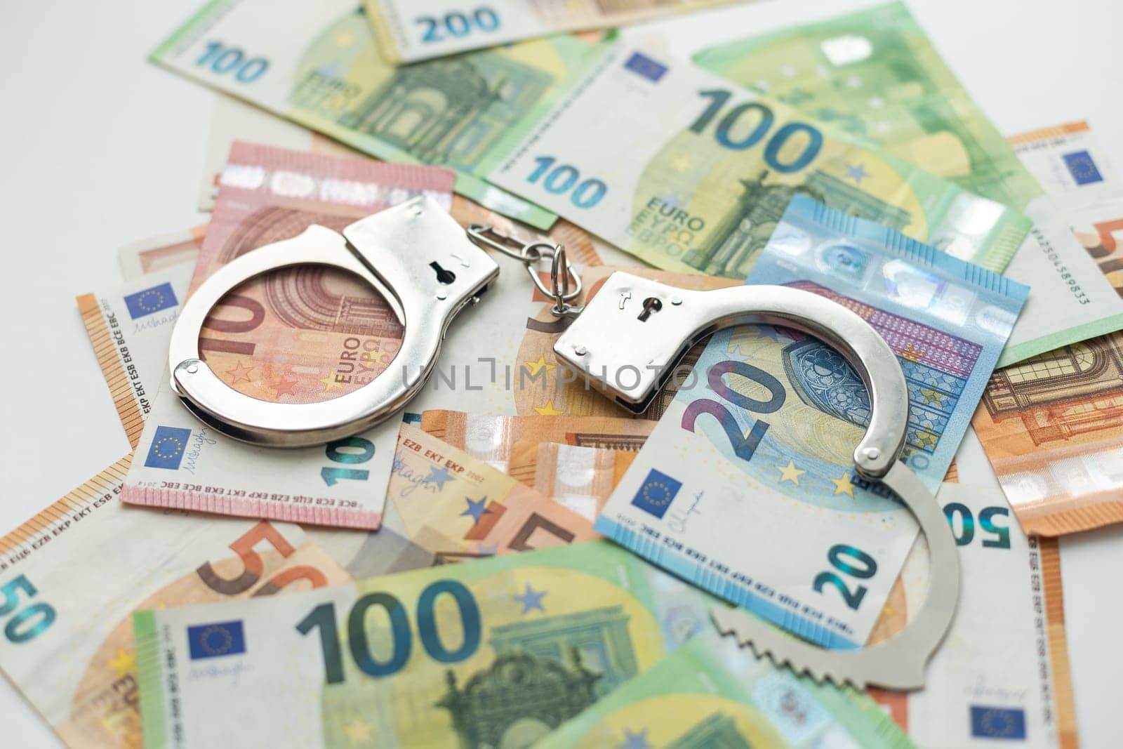 Police handcuffs lies on a set of green monetary denominations of 100 euros. A lot of money forms an infinite heap. High quality photo