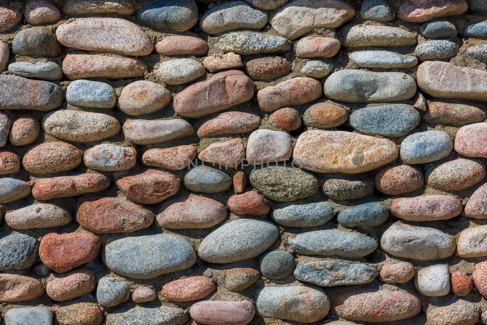 wall made of many colorful round stones under direct sun light, full-frame background and texture.