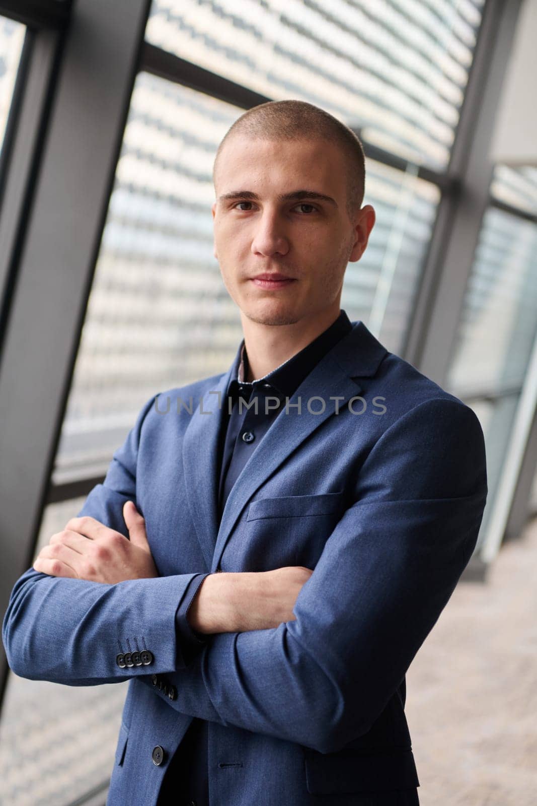 A young businessman exudes confidence and authority as he stands with crossed arms in the heart of his bustling factory, symbolizing leadership and success in the industrial world