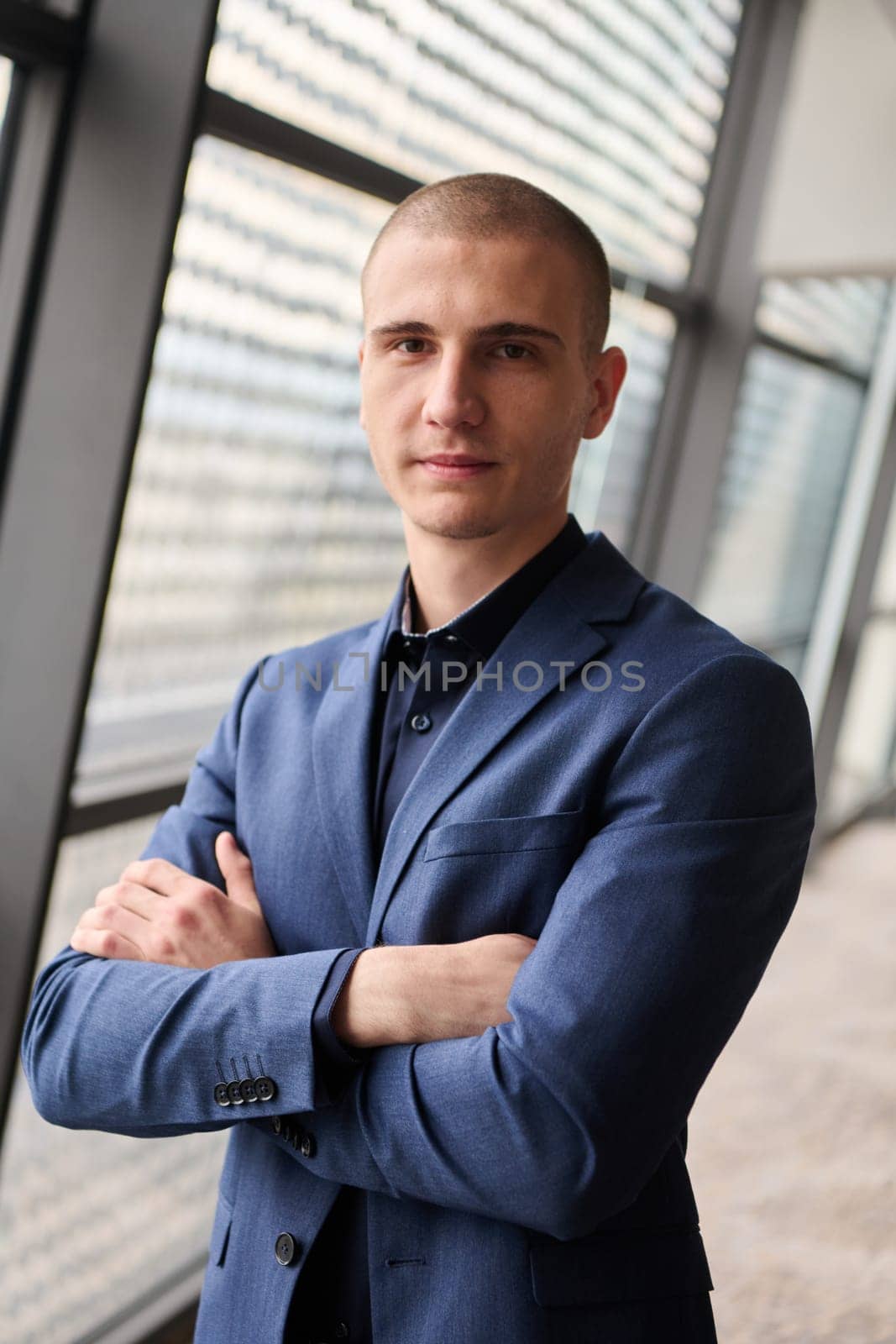 A young businessman exudes confidence and authority as he stands with crossed arms in the heart of his bustling factory, symbolizing leadership and success in the industrial world