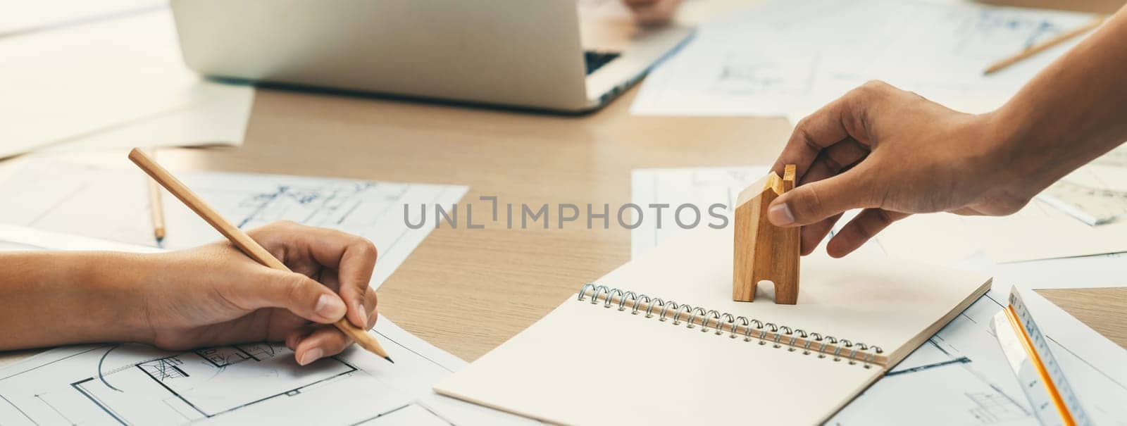 Professional architect hand draws a blueprint on table with architectural document and wooden block scatter around at office. Design and Planing concept. Focus on hand. Closeup. Delineation.