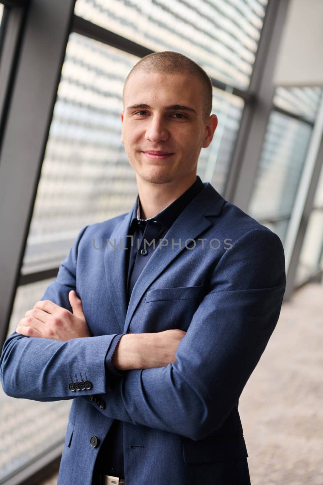 A young businessman exudes confidence and authority as he stands with crossed arms in the heart of his bustling factory, symbolizing leadership and success in the industrial world