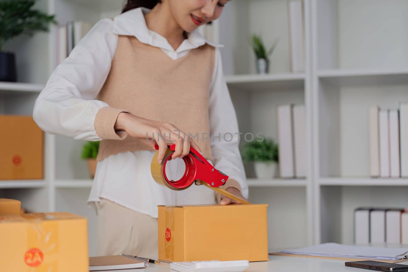 Young business entrepreneur sealing a box with tape. Preparing for shipping, Packing, online selling, e-commerce concept by itchaznong