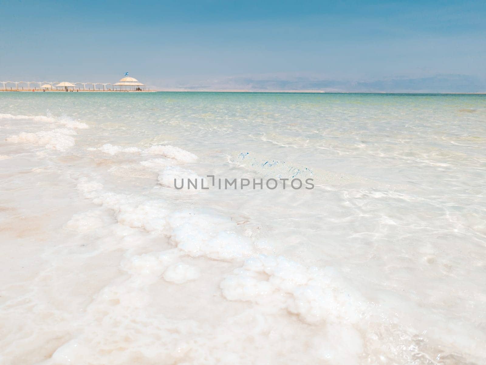 Landscape view on Dead Sea salt crystals formations, clear cyan green calm water at Ein Bokek beach, Israel