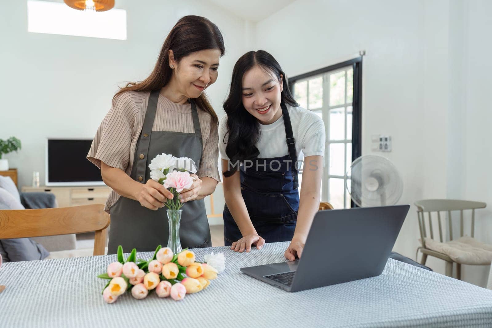 mother and daughter arrange flowers together as a hobby. mother and daughter spend free time doing flower arranging activities together and looking at laptop by itchaznong