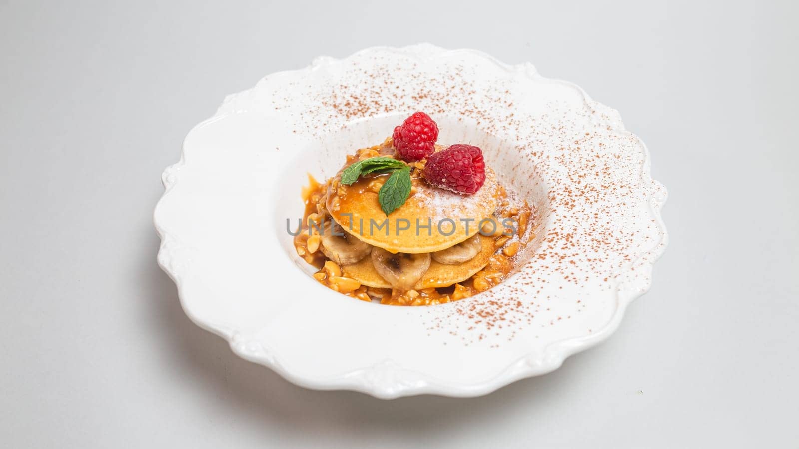 Delicious pancakes with banana-raspberry filling and maple syrup on a white background by Pukhovskiy