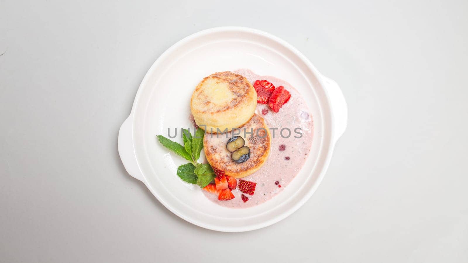 Round, fluffy cottage cheese pancakes topped with vibrant strawberries and blueberries on a white plate, perfect for a delicious breakfast.