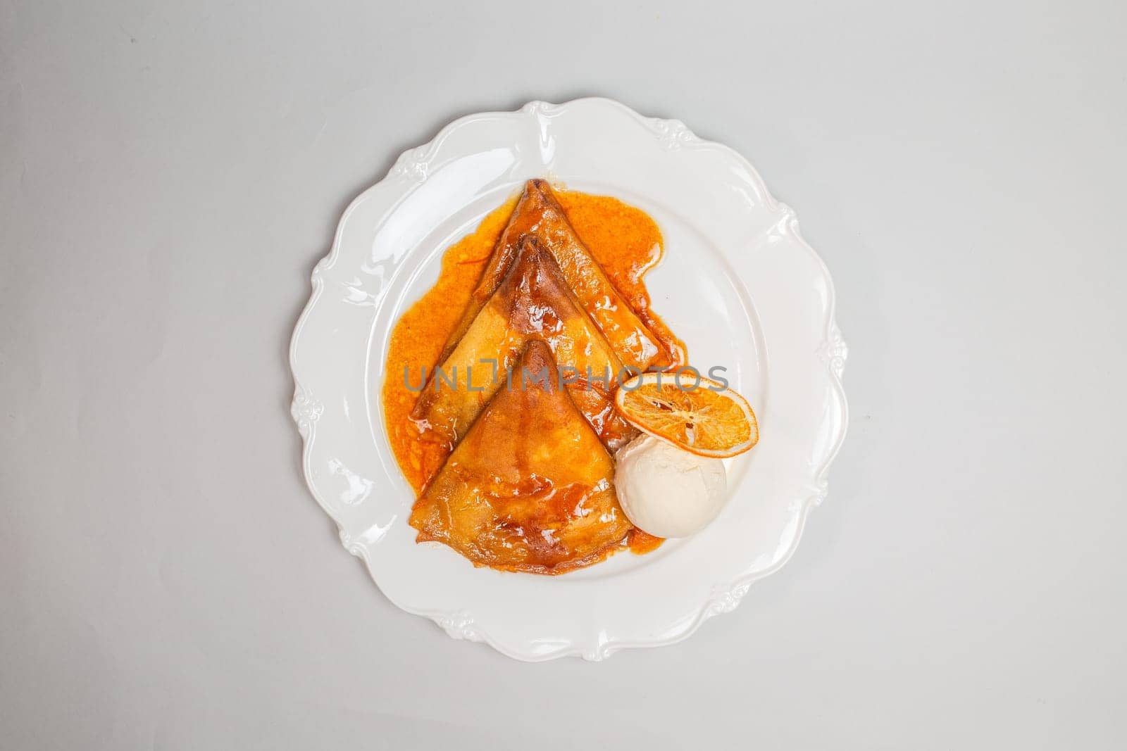 A decadent dessert of crepes topped with orange sauce and a scoop of vanilla ice cream, isolated on a white background.