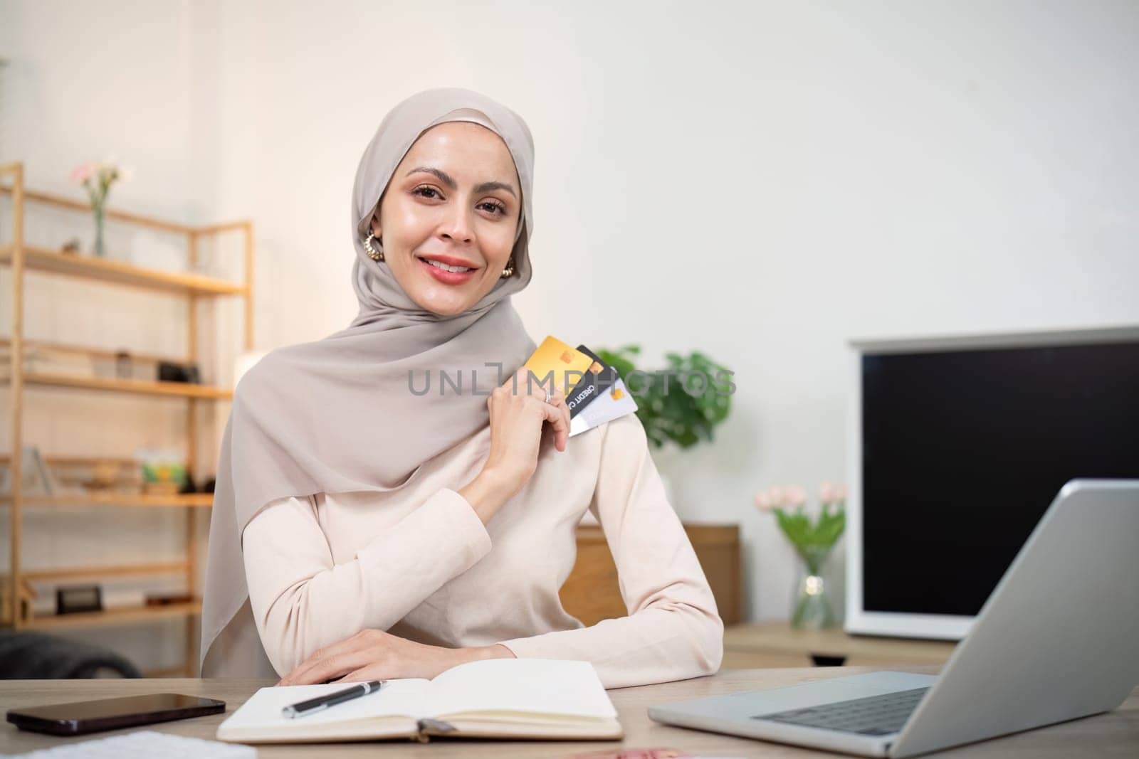 Young woman using laptop at home shopping online. Muslim woman wearing hijab using laptop and holding credit card. Internet banking concept. Muslim woman online shopping.