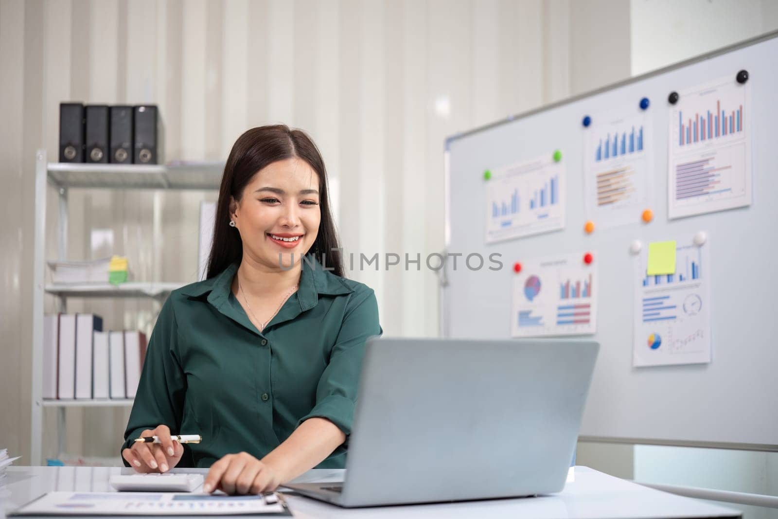 Beautiful determined business woman working using laptop and calculator calculating turnover in modern office.
