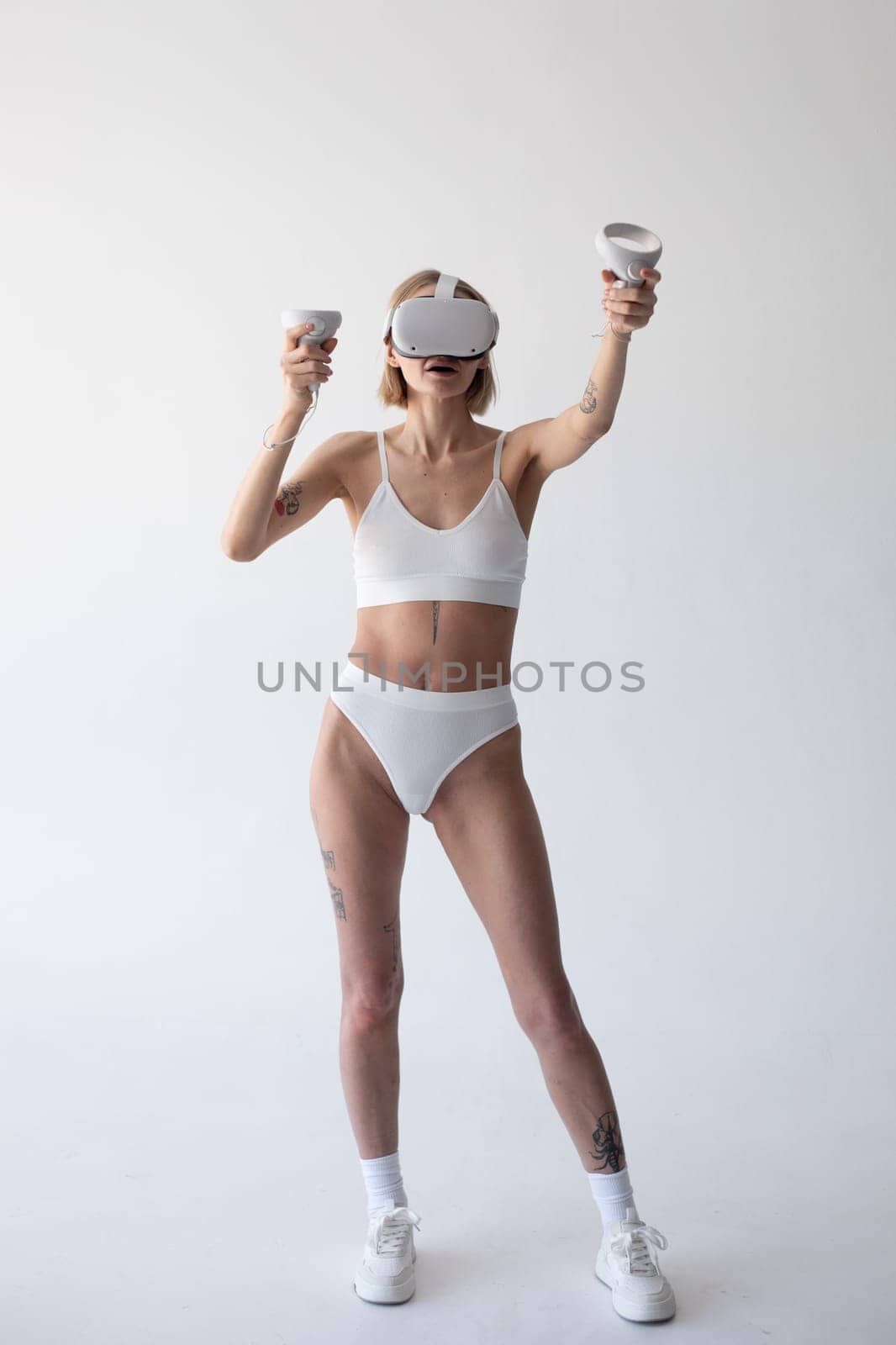 Beautiful thin girl in white shorts and a top in a virtual reality helmet posing on a white background. High quality photo