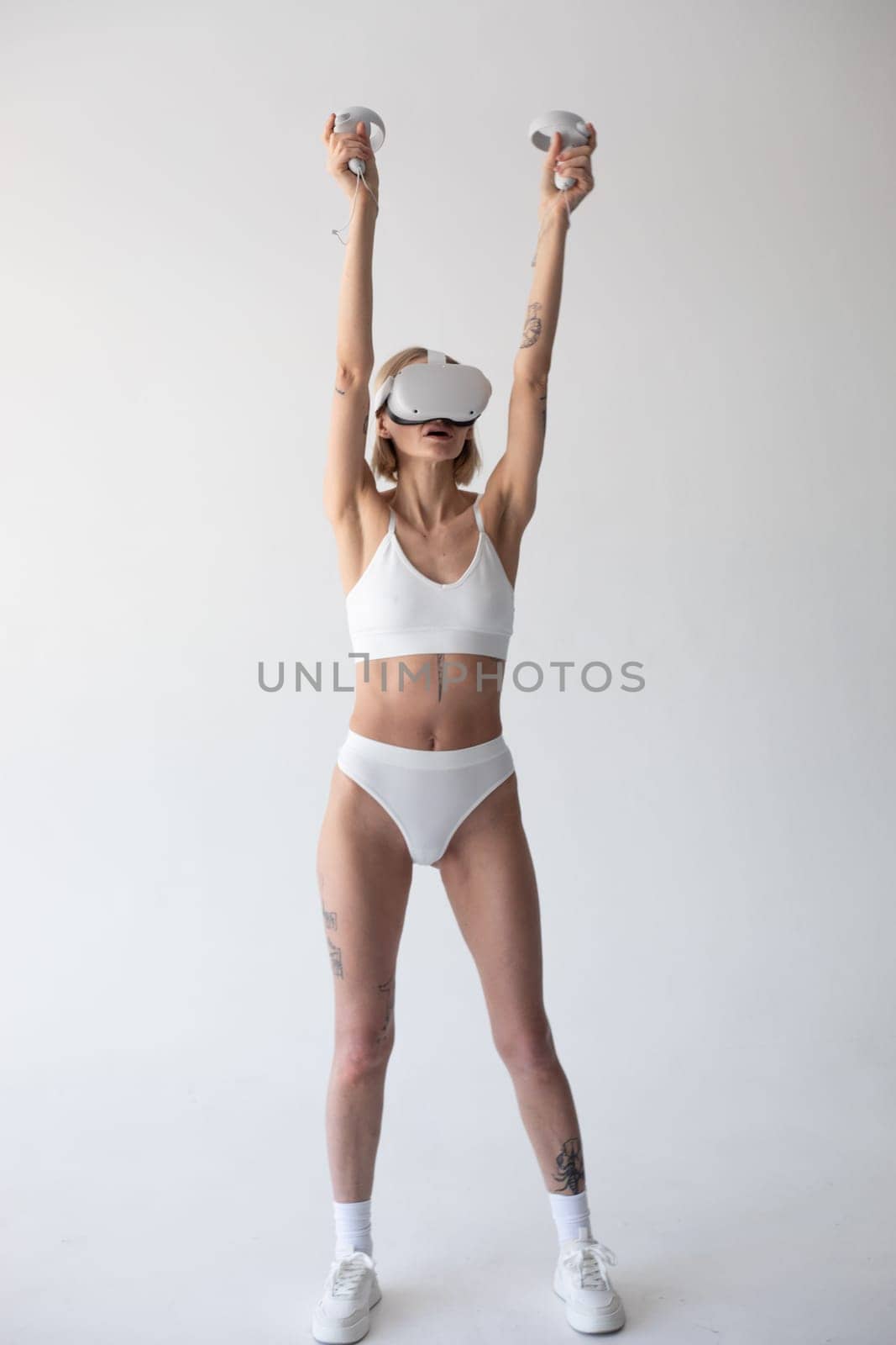 Beautiful thin girl in white shorts and a top in a virtual reality helmet posing on a white background by Freeman_Studio