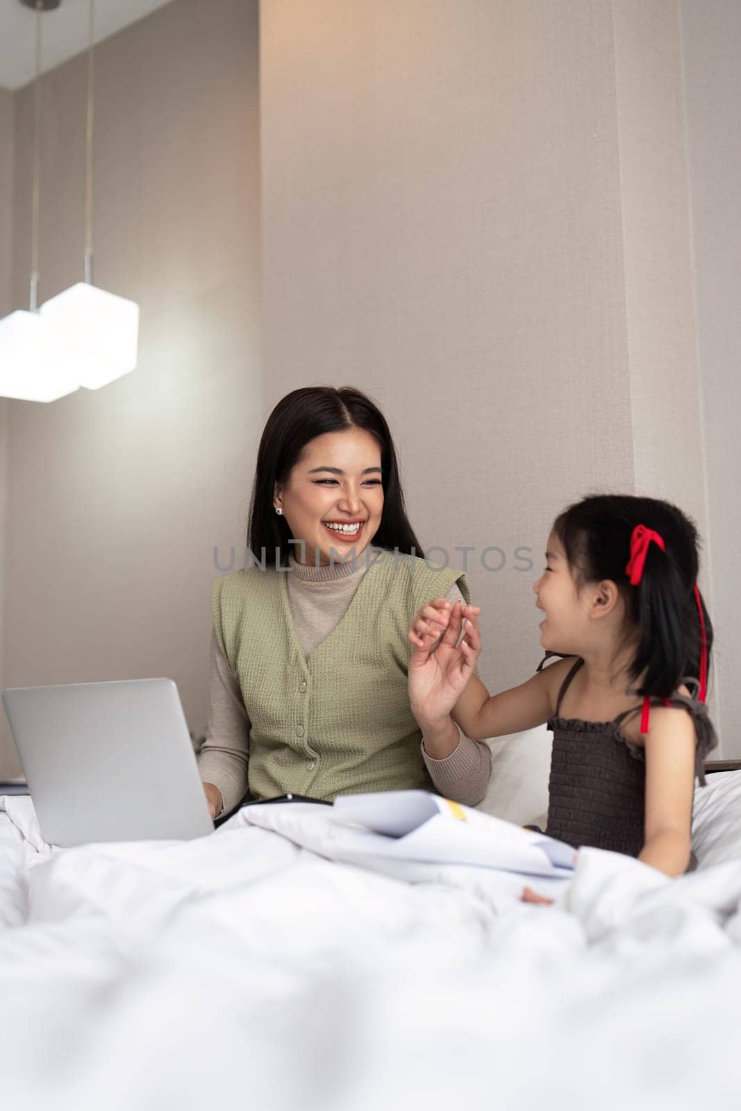 Mom work from home with children. Mother working on bed laptop in bedroom with child daughter. Funny authentic lifestyle family moment by nateemee