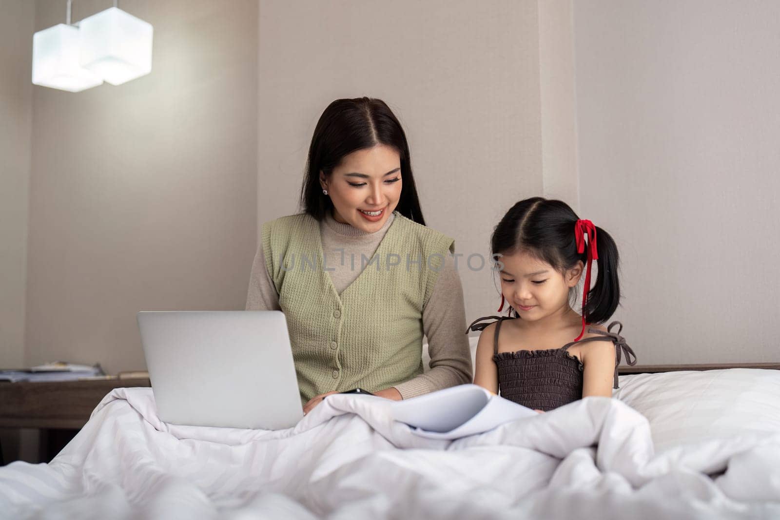 Mom work from home with children. Mother working on bed laptop in bedroom with child daughter. Funny authentic lifestyle family moment by nateemee