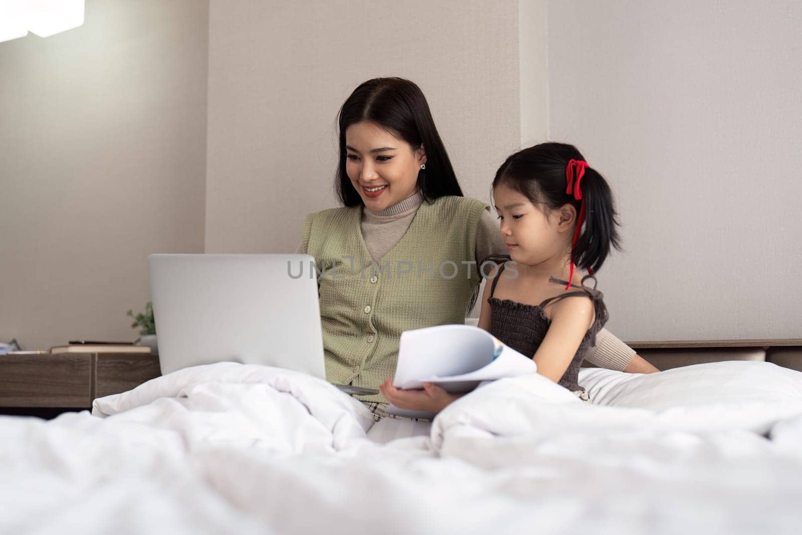 Mom work from home with children. Mother working on bed laptop in bedroom with child daughter. Funny authentic lifestyle family moment.