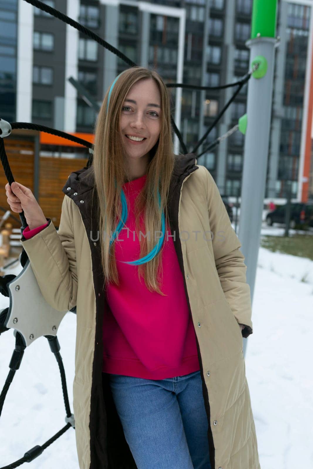 A woman is standing in a snowy landscape, holding a ski pole in her hand. She is dressed in winter attire and appears to be preparing for skiing.