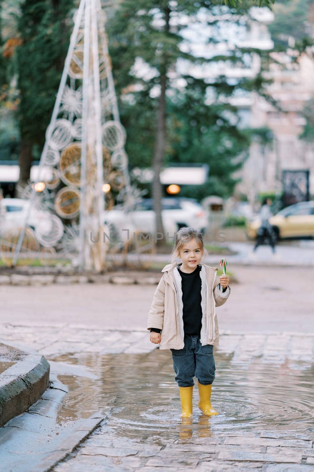Little girl with a striped candy cane walks through a puddle in the park. High quality photo