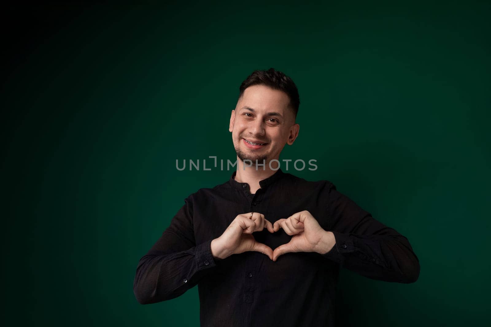 A man is forming a heart shape with his hands, fingers touching to create the recognizable symbol of love and affection. The background is simple, allowing the focus to remain on the gesture he is making.