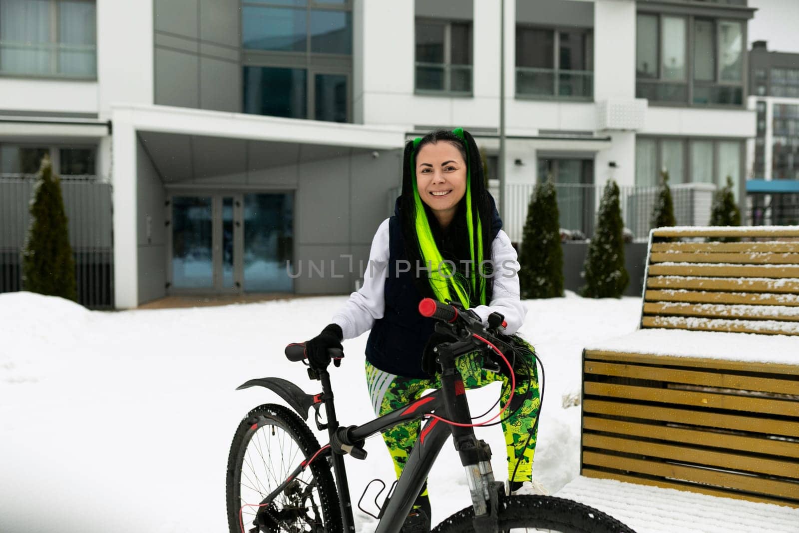 A woman standing next to a bicycle in a wintery landscape covered in snow. She is dressed warmly and appears to be inspecting the bike, which is slightly dusted with snow.