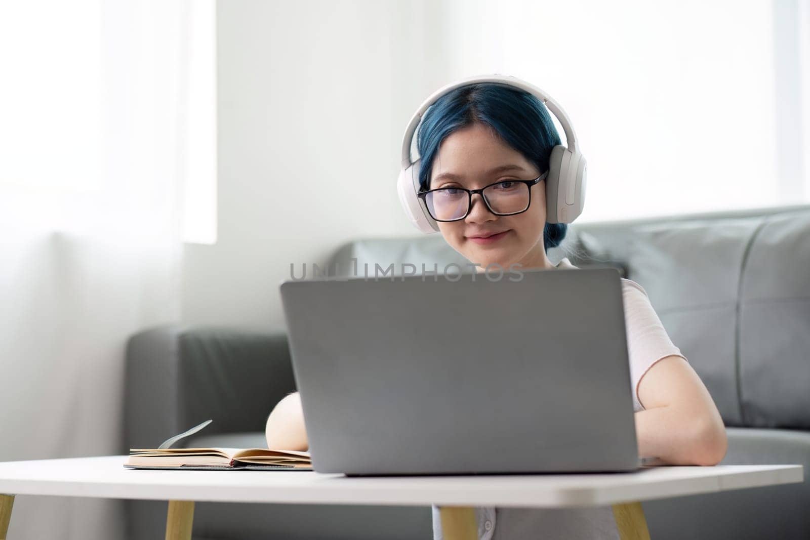 Happy young woman teenage wearing headphones writing note. student online learning class study online video call zoom teacher with laptop and book by nateemee