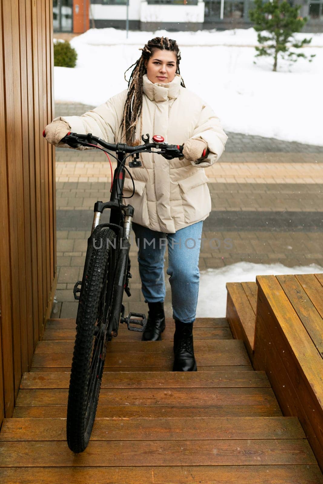 A woman with dreadlocks is carefully navigating a bike down a flight of stairs. She is holding onto the handlebars and balancing the bike as she descends each step. Her focused expression shows determination in safely completing this unconventional task.