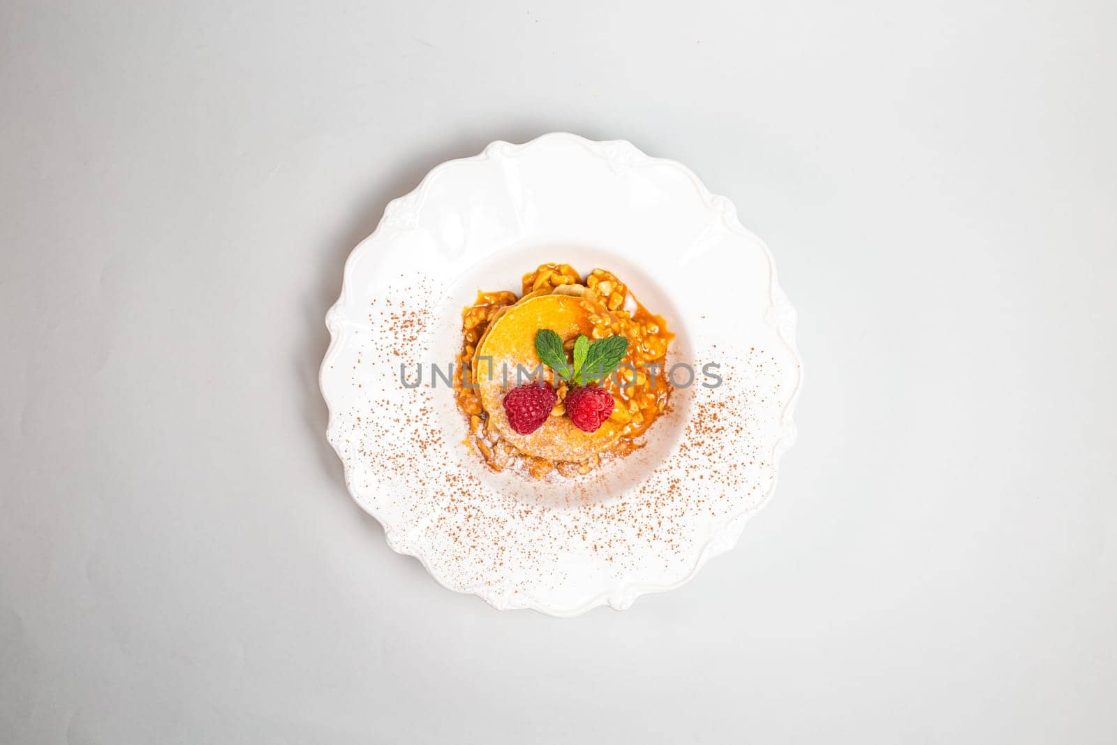 Fluffy pancakes with raspberries and mint leaves on a white plate against a clean white background. Close-up shot.