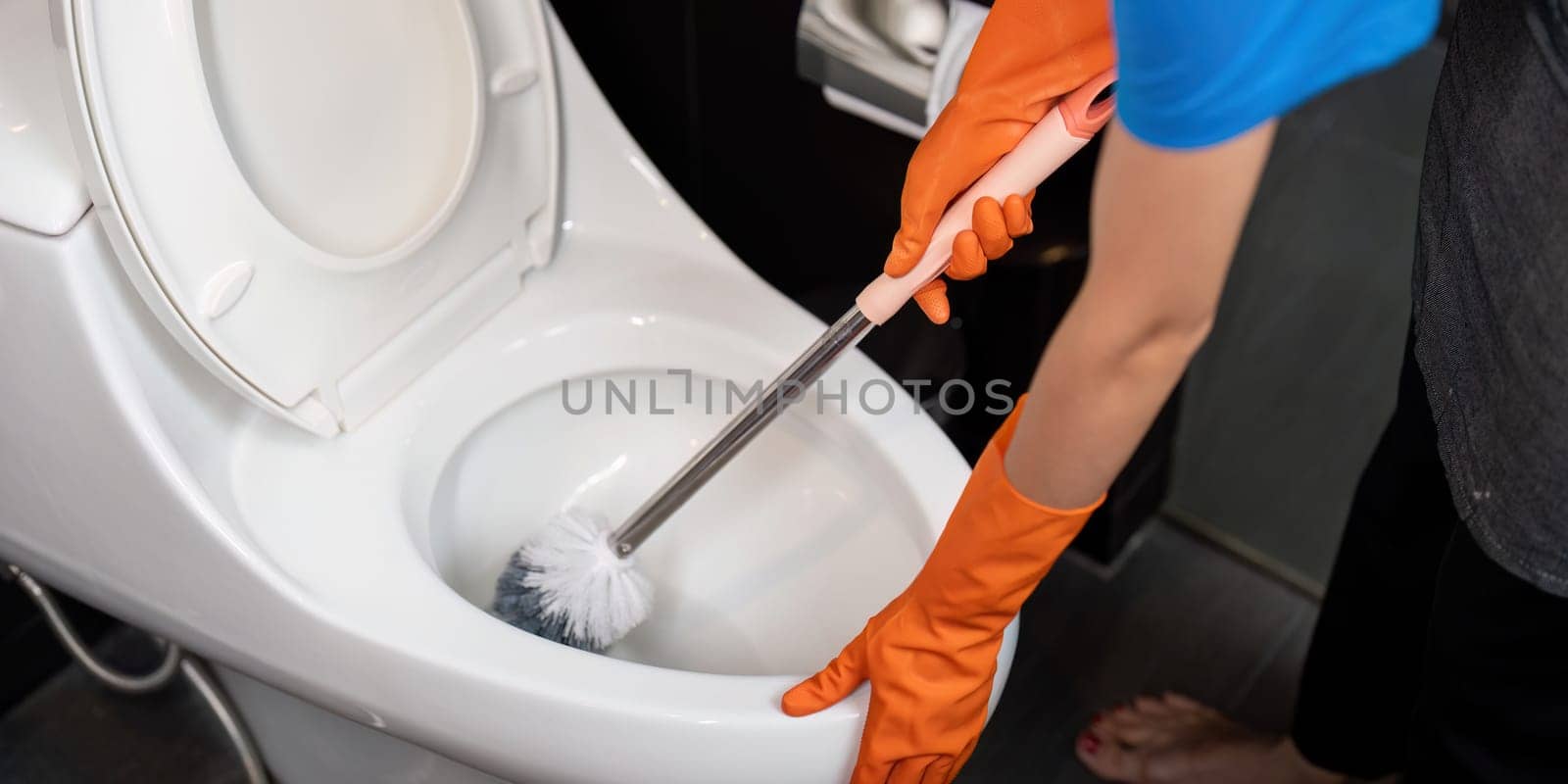Professional cleaning service company employee in rubber gloves cleaning a toilet bowl in bathroom.
