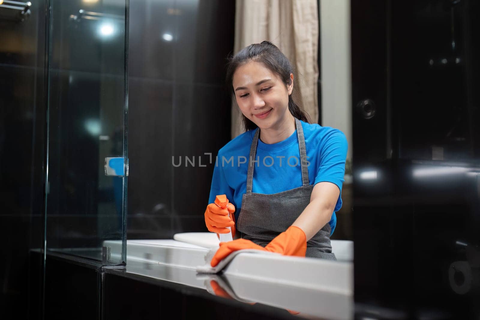Professional cleaning service company employee in rubber gloves cleaning and detergent spray in bathroom.
