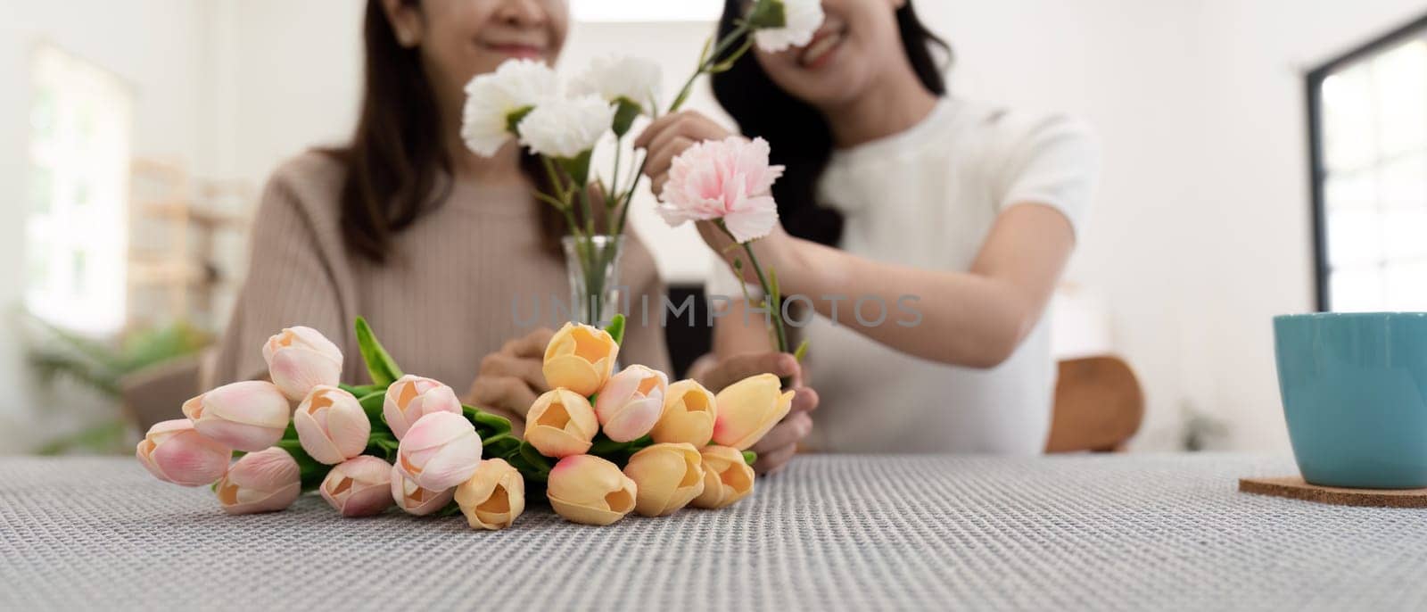 Senior mother and adult daughter happy on the table while arrange flowers in a vase together. Technology and lifestyle concept. Happy time together.
