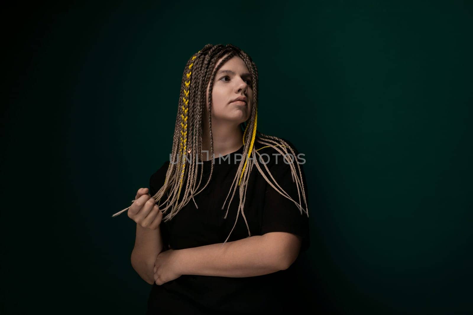 A woman with dreadlocks standing confidently in front of a bright green wall. She is looking directly at the camera with a relaxed expression.