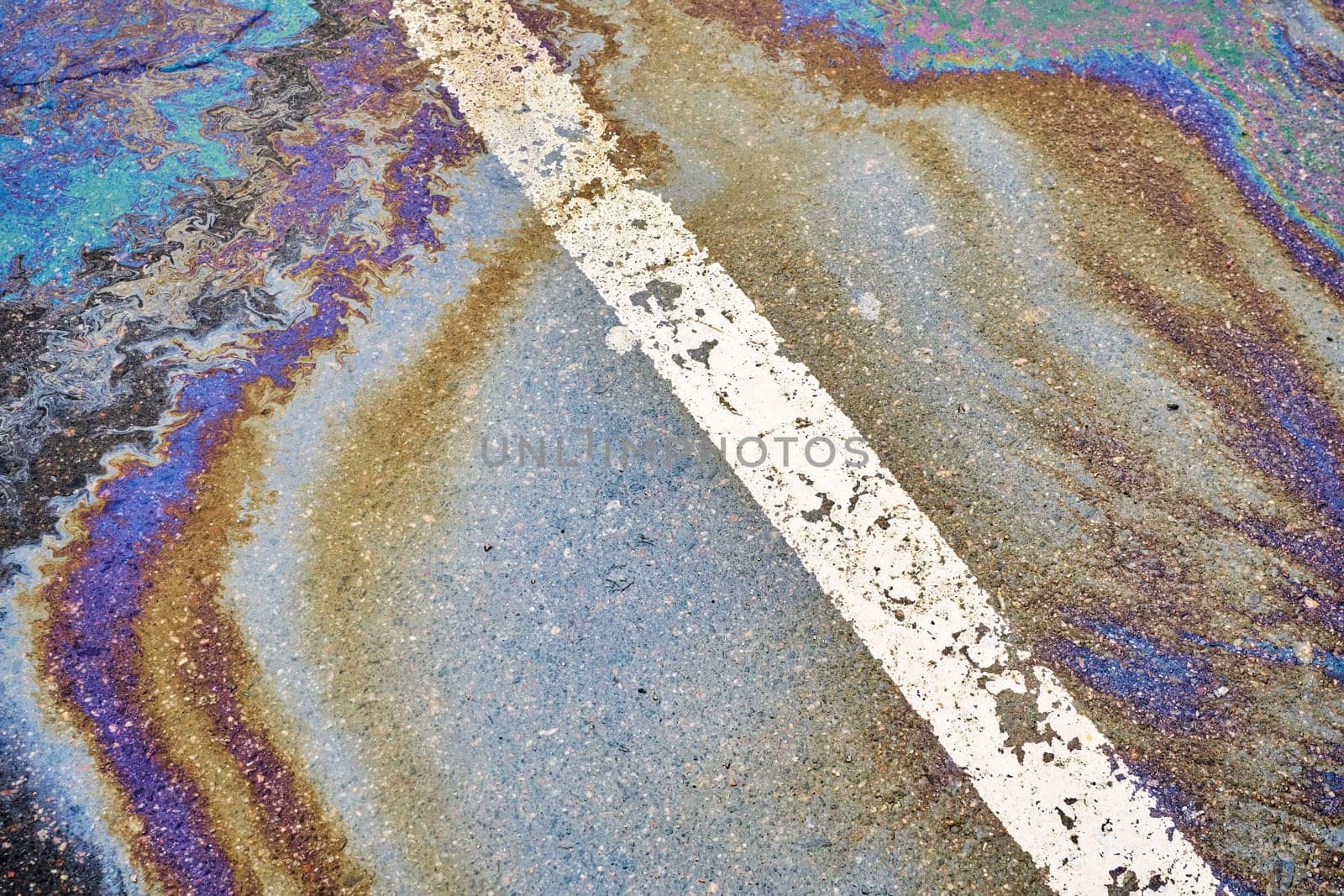 Oil spill on wet asphalt, parking lot with dividing line.