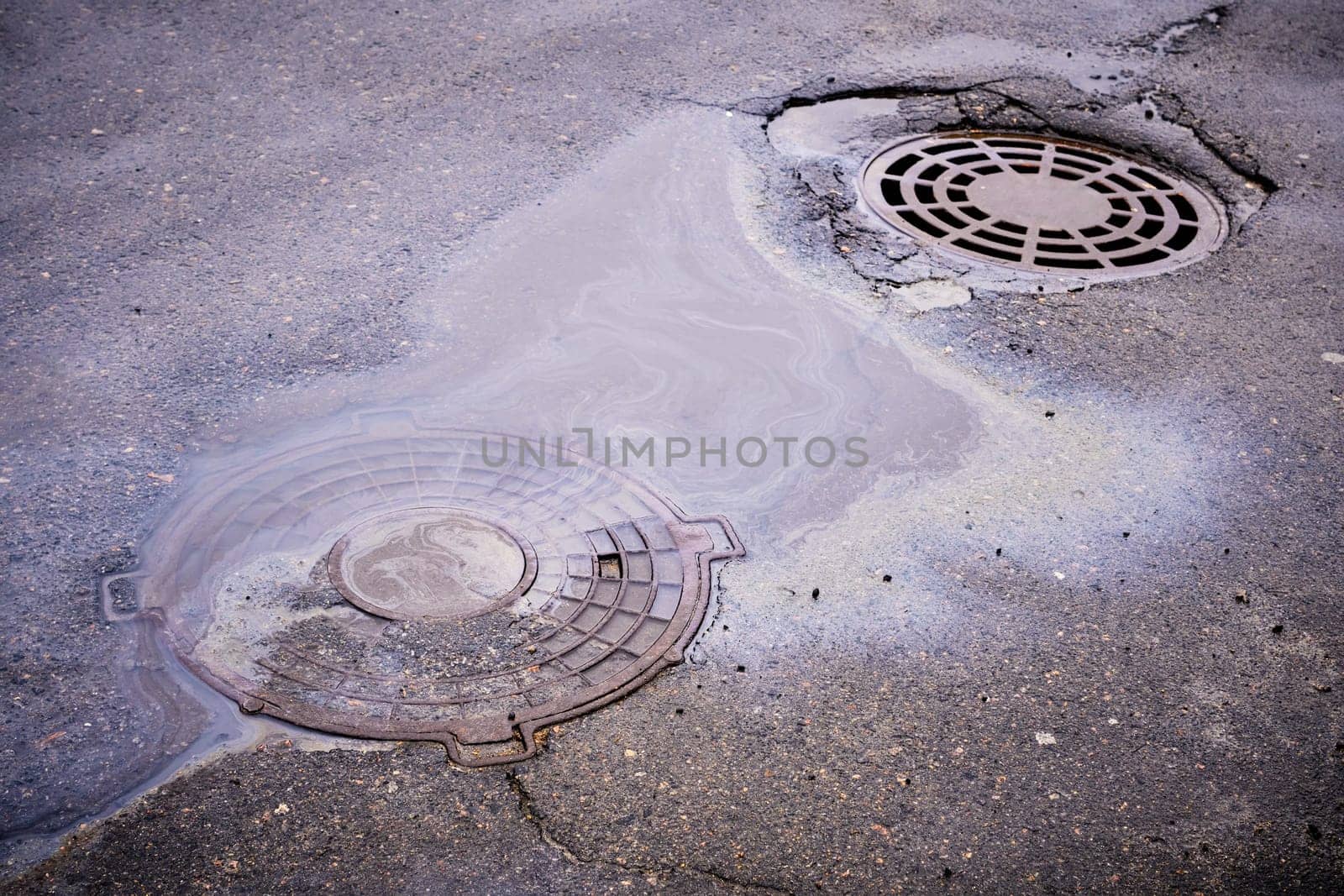 The oil slick on the asphalt road is contributing to water pollution as it drains into the storm drain