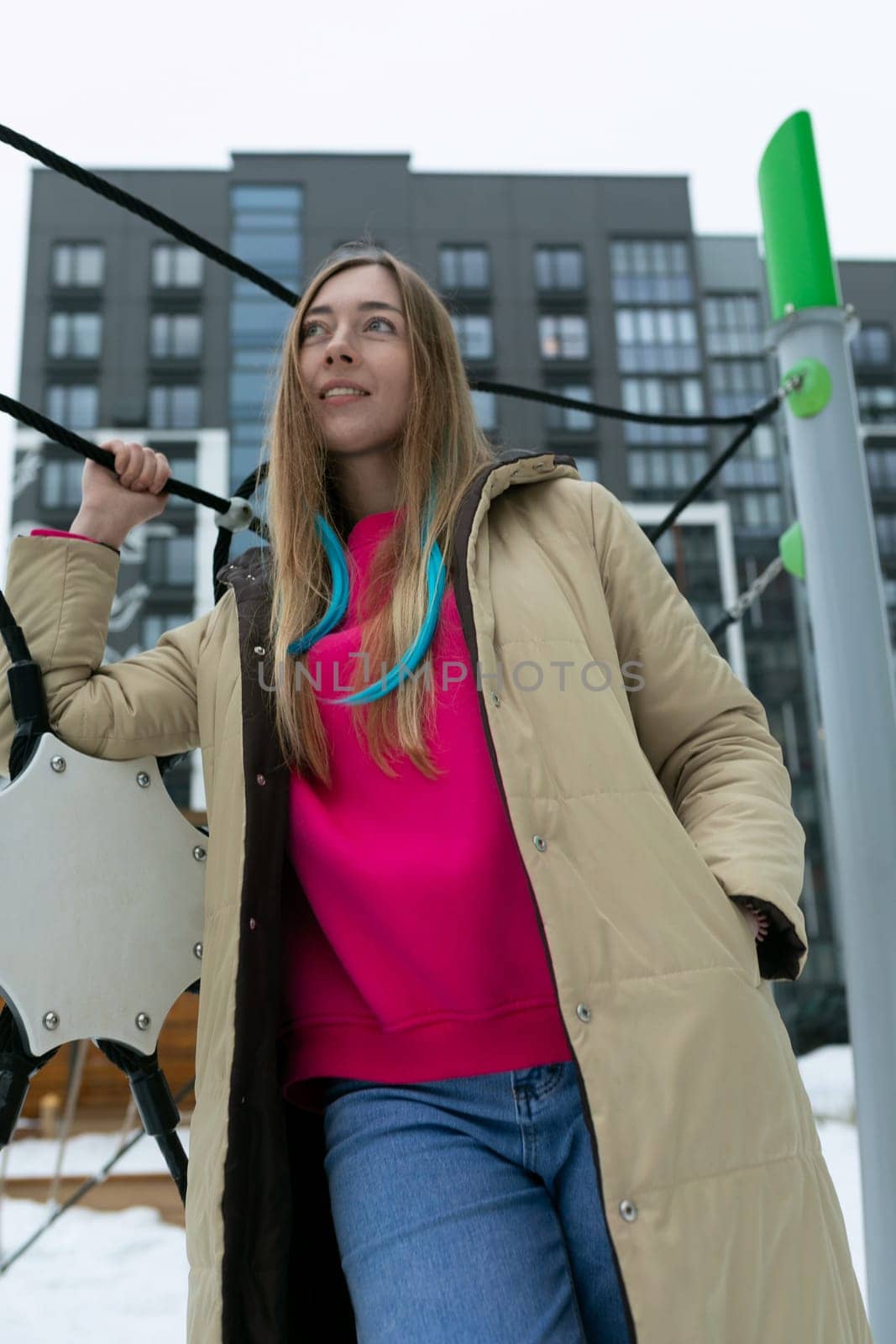 A woman wearing a pink shirt and coat standing outdoors. She is casually dressed and appears to be in a public space.