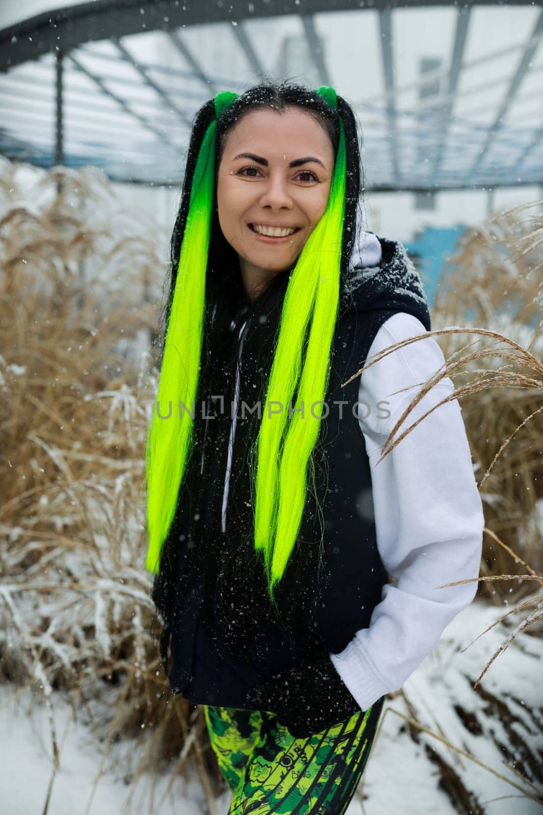 A woman with vivid green hair stands in the midst of a snowy landscape, her striking hair contrasting against the white snow. She gazes ahead, embodying a sense of strength and resilience in the cold winter setting.