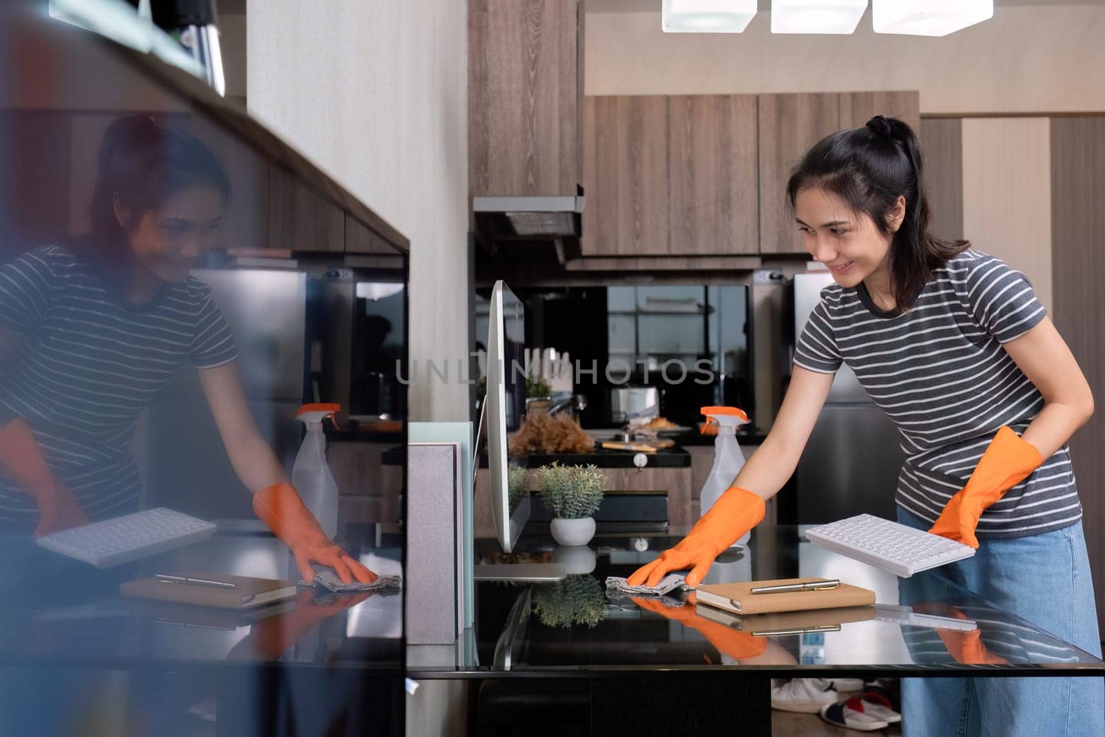 A beautiful young housekeeper wears orange gloves and uses a cloth to clean the table and living room..