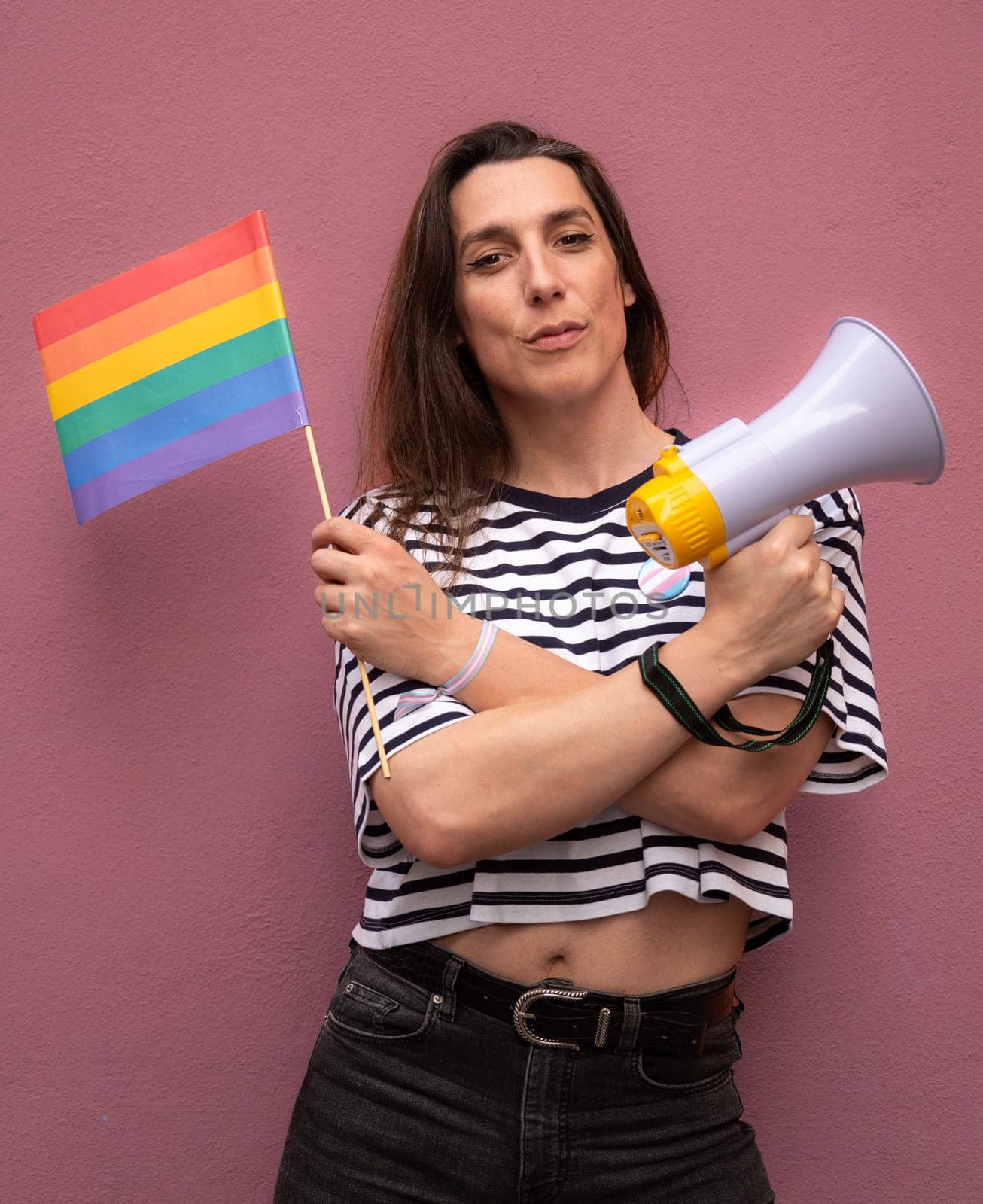 Transsexual woman looking at camera and holding a rainbow flag and a megaphone to support LGBTQ community as activist.