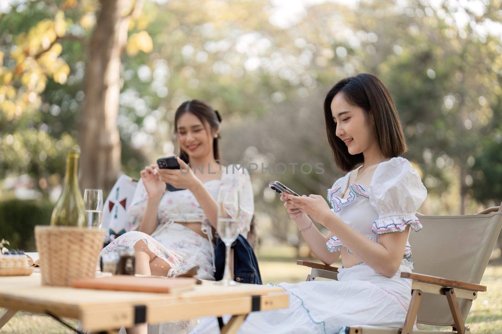 Two best friends sit on the phone and chat while having an outdoor picnic at the park. by wichayada