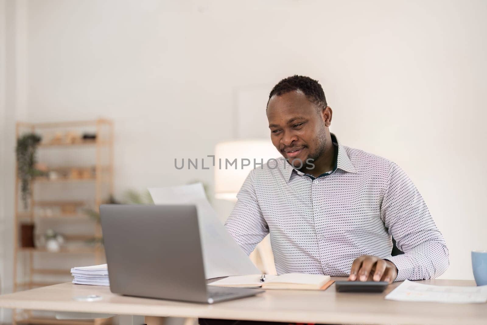 Young African American businessman uses laptop to work on white wooden table in office room. by wichayada