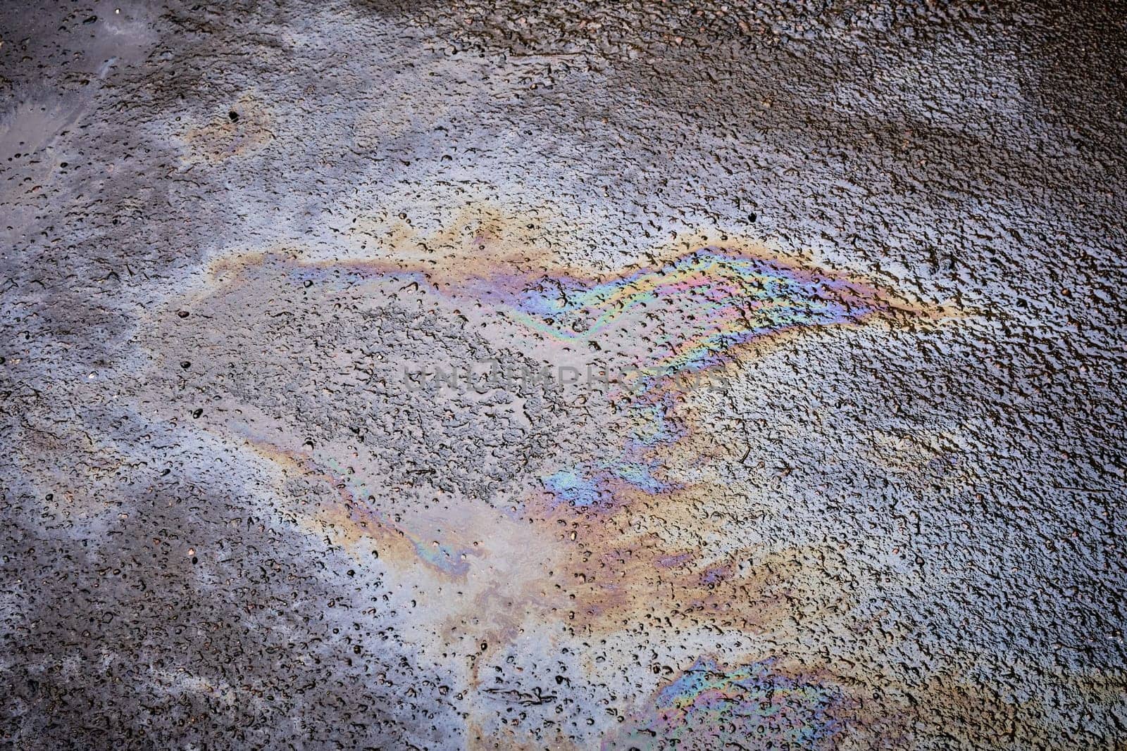 Pollution of wet asphalt with fuel or oil stains against the background of rain.