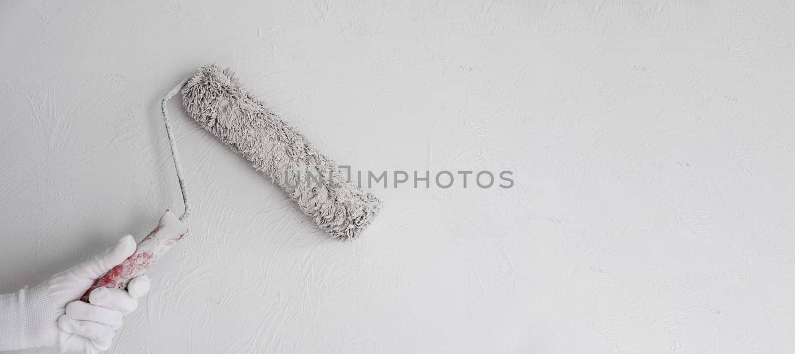 Painting a bare wall with a roller with white paint. Apartment painting by AnatoliiFoto