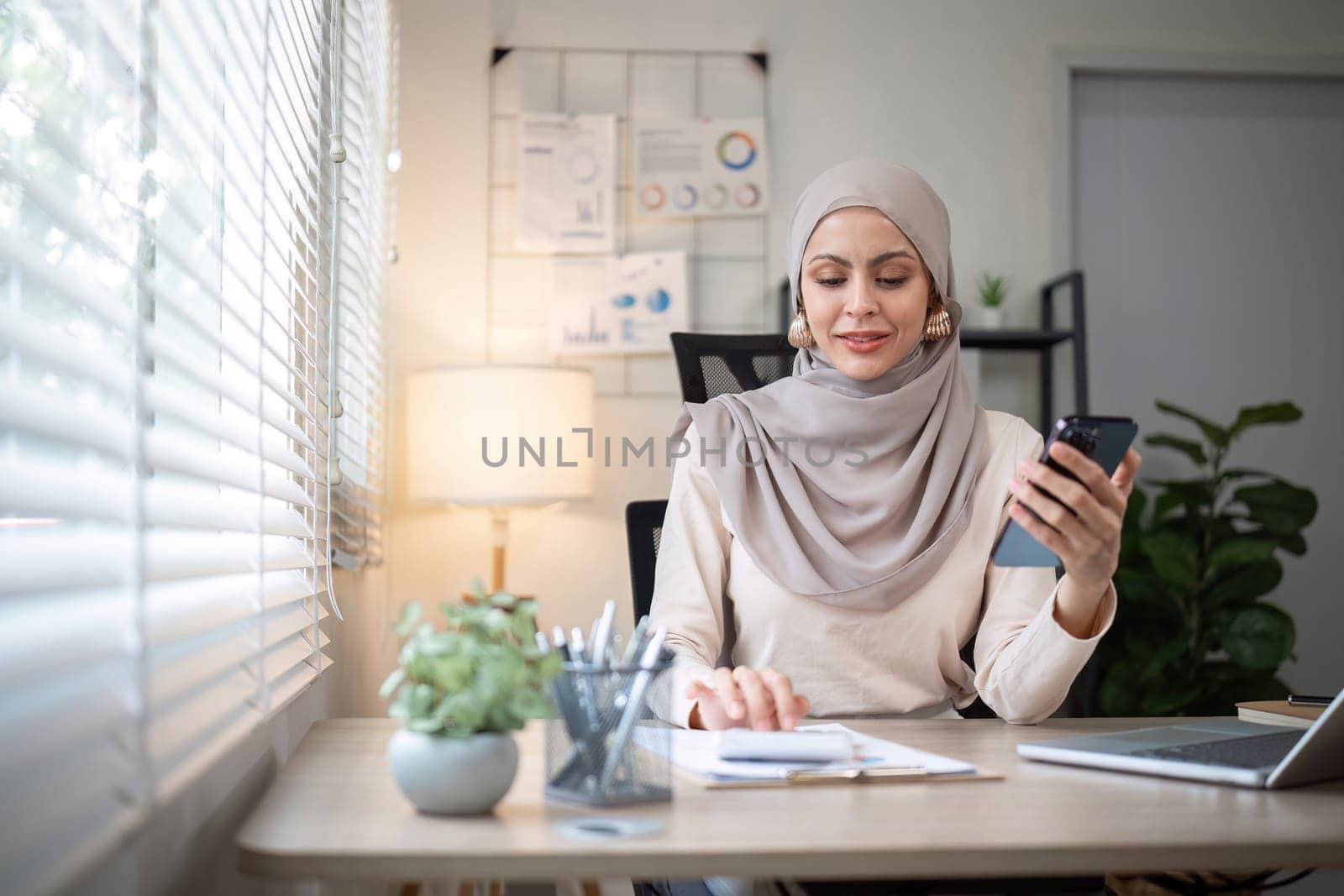 Happy Muslim businesswoman wearing hijab at work Use your laptop and smartphone to work on finance and marketing in the office. by wichayada