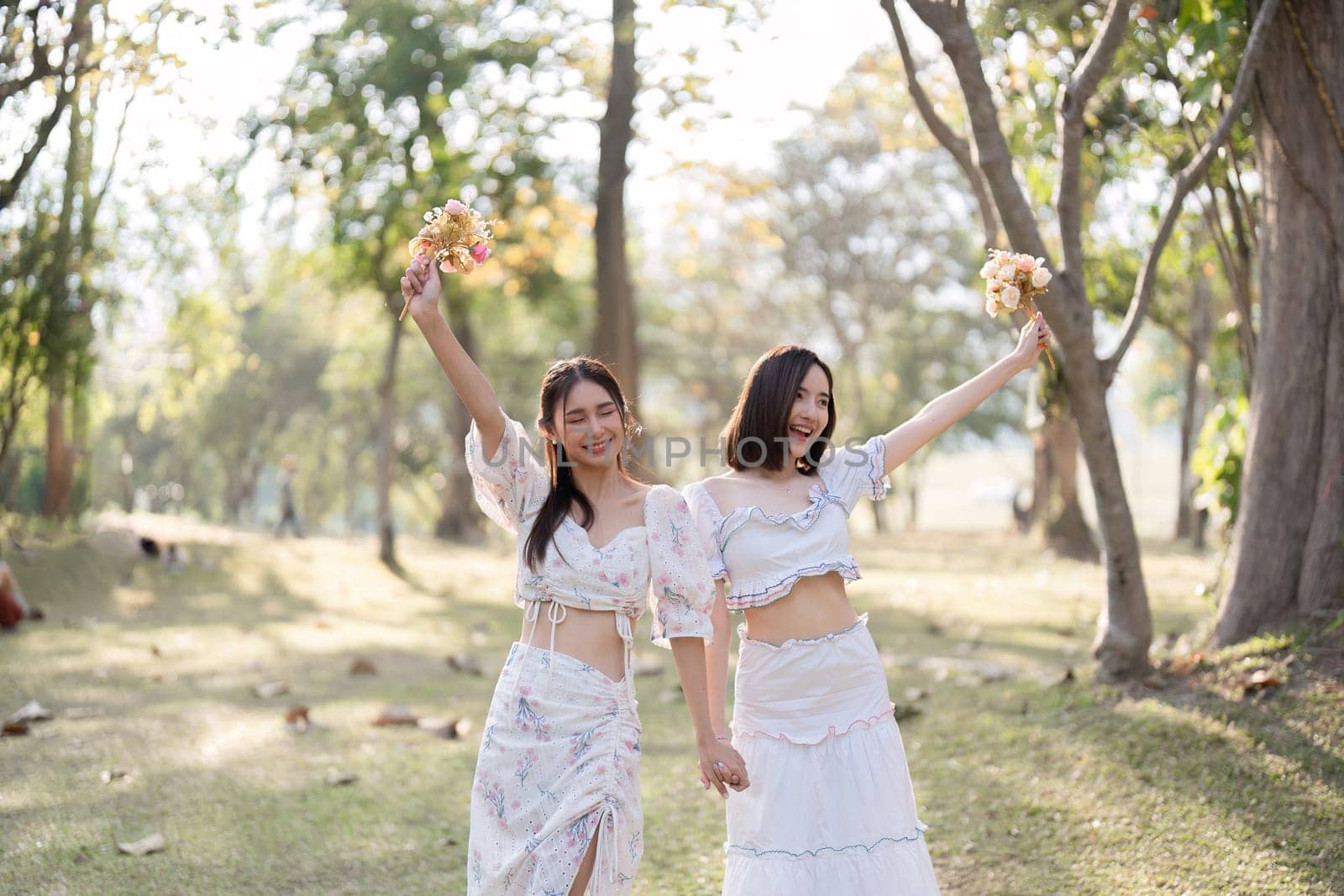 Two young friends walk together in a beautiful public place, admiring nature and holding colorful flowers..