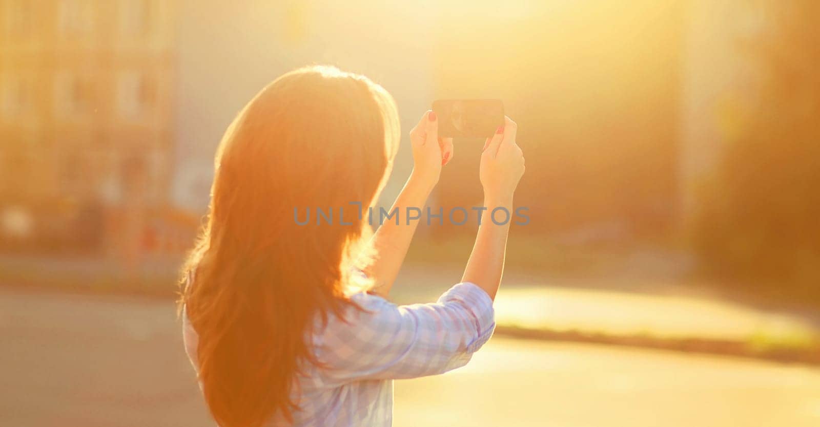 young woman taking selfie with mobile phone in sunny summer on city street