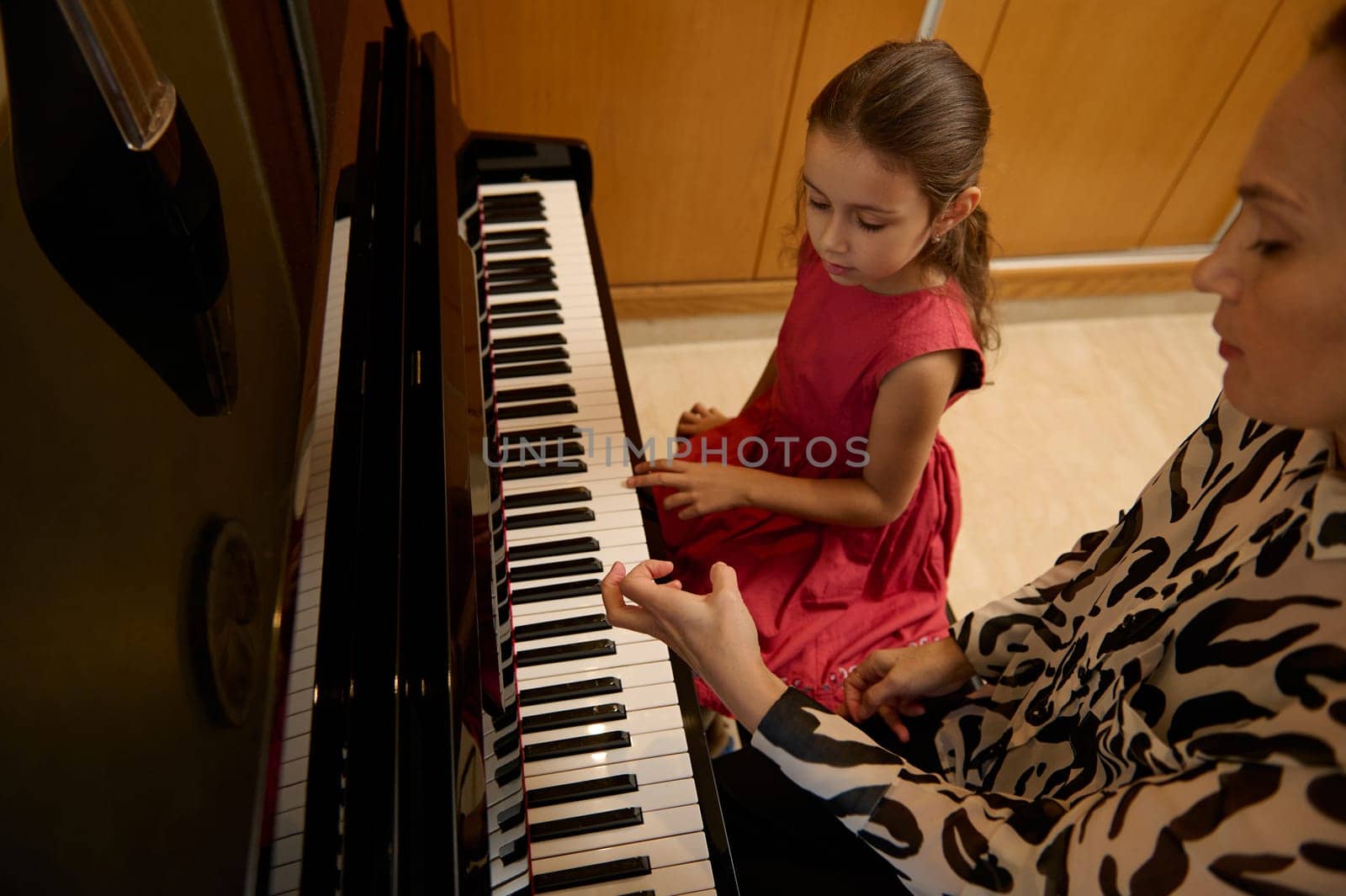 Little child girl having a piano lesson with her teacher. Female pianist explaining the correct position of hands on piano keys. Musical education and talent development in progress