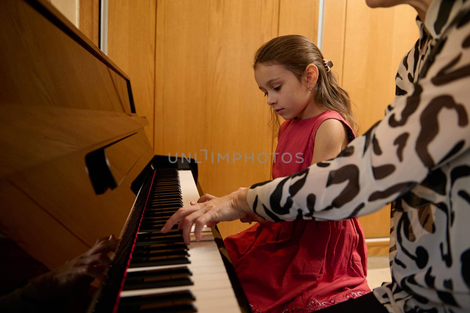 Little kid girl having a piano lesson with her teacher at home. Little child girl putting her fingers on ebony and ivory keys, creating rhythm of sound, composing melody and singing Christmas song