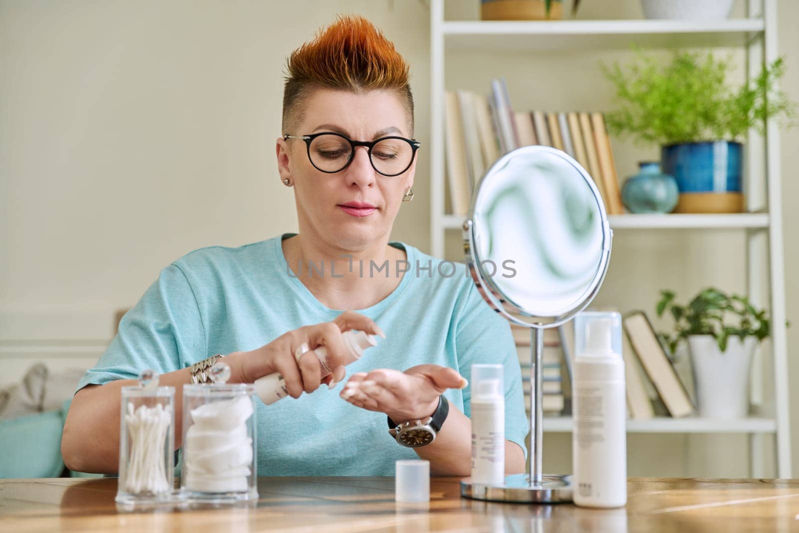 Middle-aged woman with a mirror taking care of her facial skin by VH-studio