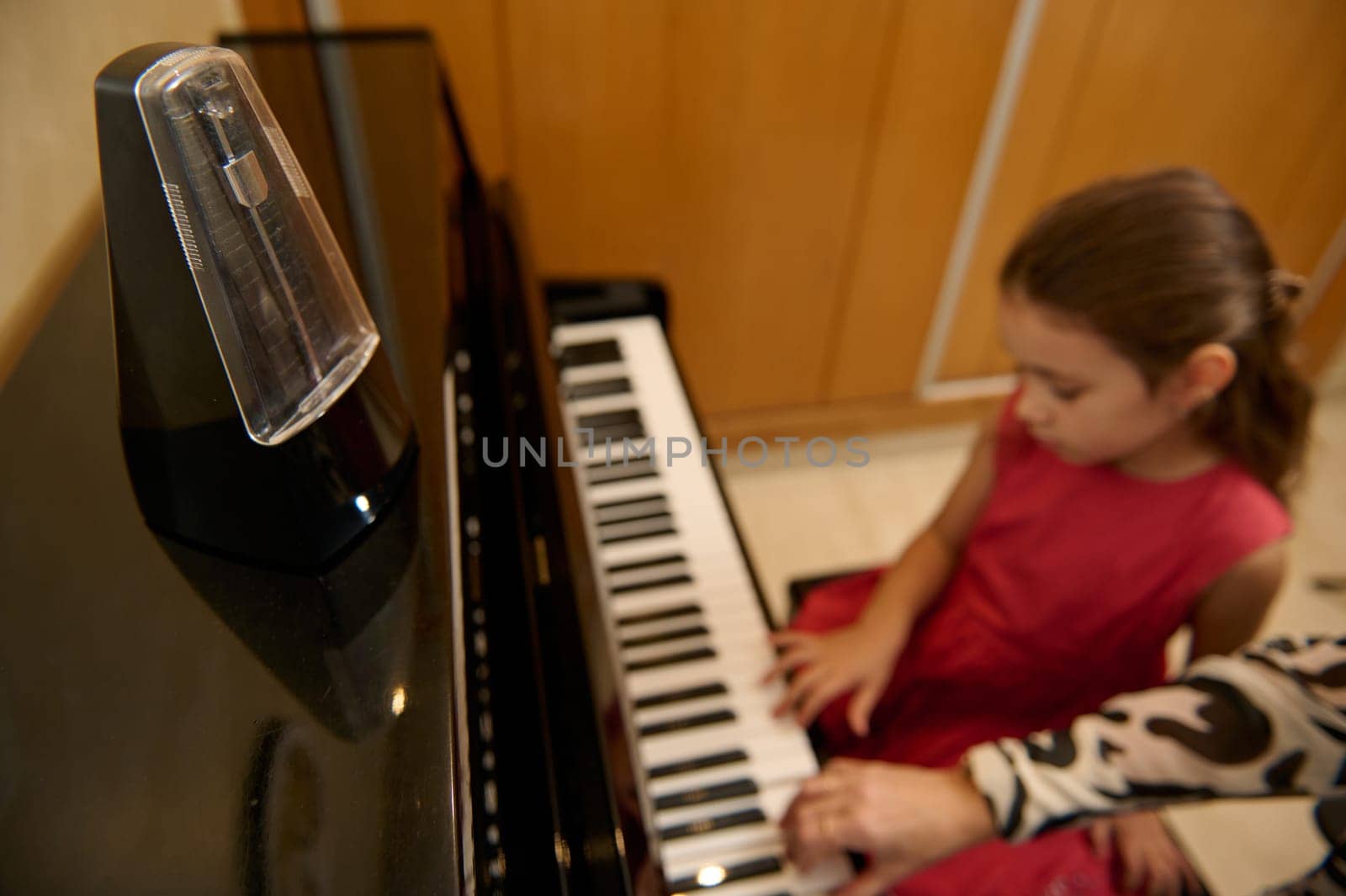 Little kid girl having a piano lesson with her teacher at home. Little child girl putting her fingers on ebony and ivory keys, creating rhythm of sound, composing melody and singing Christmas song by artgf