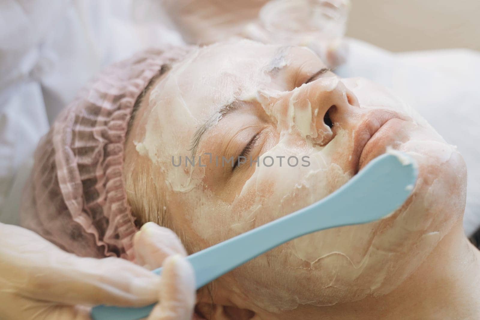 A woman is having a facial mask applied to her face in a spa setting. The skincare professional is gently smoothing on the mask for a revitalizing treatment.